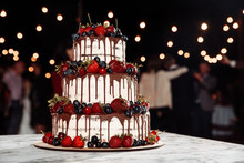 Beautiful And Delicious High Three Tier Cake, Which Is Decorated With Various Berries. Garlands On The Sides Of The Cake. Side View. Bokeh