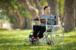 © chayathon2000 - Asian senior woman sitting on the wheelchair and reading book in the park garden smile and happy face