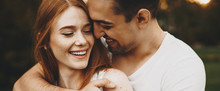 Close Up Portrait Of A Charming Young Couple Laughing While Man Is Embracing Her Girlfriend Against Sunset Outdoor In Park.
