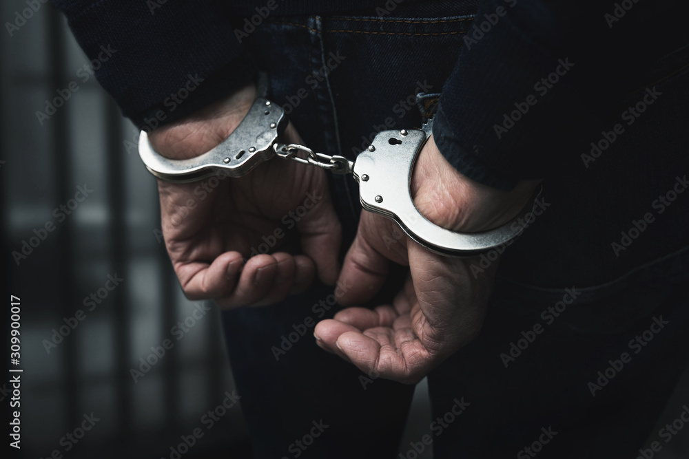 arrested man with cuffed hands behind prison bars - obrazy, fototapety, plakaty 