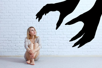 Woman sitting on the floor and looking on imaginary big hands with claws.