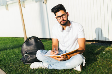 Portrait of handsome indian tourist man wearing glasses reading a book at the park on a day.