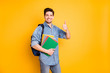 Photo of cheerful positive handsome man showing you thumb up holding copybooks with backpack behind smiling toothily isolated vivid color background