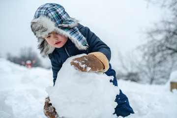 Beauty Winter child with snowman in frosty winter Park. Winter children in frosty winter Park. Portrait of little boy child in snow Garden make big snowball.