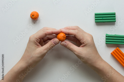 Fotografía Woman hands holding small orange fruit made from polymer clay on white backgroun