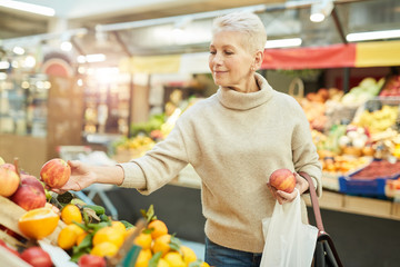 Waist up portrait of beautiful senior woman choosing fresh fruits at farmers market, copy space