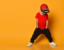 Young Guy Boy In A Red T-shirt And Dark Pants, White Sneakers And A Funny Cap Posing On A Free Copy Space On A Yellow Background