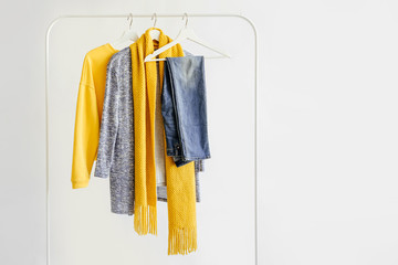 Wall Mural - Female clothes in yellow and blue color on hanger on white background. Jumper, shirt and scarf. Spring/autumn outfit. Minimal concept.