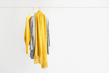 Wall Mural - Female clothes in yellow and blue color on hanger on white background. Jumper, shirt and scarf. Spring/autumn outfit. Minimal concept.