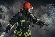 Brave Extinguisher Or Fireman Dressed In Dark Protective Suit Uniform, With Helmet On Head, Using Ropes, Hammer And Other Special Equipment At Work