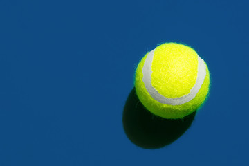 One yellow tennis ball laying on court in classic blue color in bright sunlight. Sports active lifestyle competition victory concentration concept. Pop art style with hard shadows