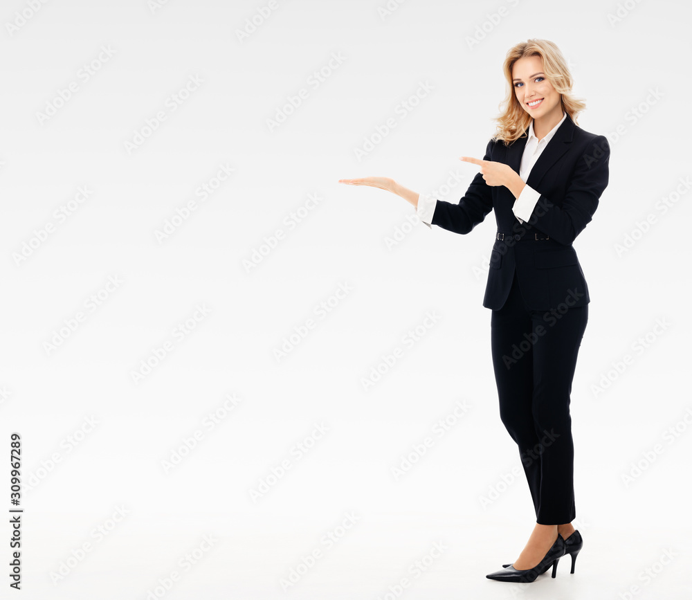 Full body portrait of happy smiling young businesswoman in black confident suit, showing something or blank copy space for some slogan or text, over grey background - obrazy, fototapety, plakaty 