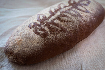 soft of brown crusty tasty loaf of bread with floral decor and flour on vintage textured tablecloth