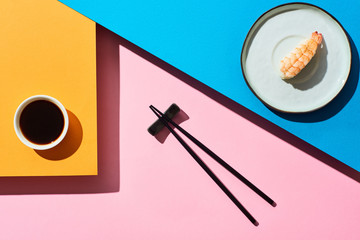 Wall Mural - top view of fresh nigiri with shrimp near soy sauce and chopsticks on blue, pink, orange background