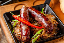 Turkish Cuisine Concept. Beef Sausages With Stewed Cabbage And Red Hot Peppers In An Iron Pan. Serving Dishes In A Restaurant. Background Image. Copy Space