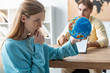 © LIGHTFIELD STUDIOS - selective focus of thoughtful young woman looking at globe while sitting near travel agent