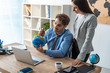 © LIGHTFIELD STUDIOS - attractive travel agent standing near colleague pointing with pen at globe