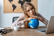 © LIGHTFIELD STUDIOS - tired travel agent leaning on globe while sitting at workplace