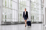 Fototapeta  - business trip, corporate and people concept - young businesswoman walking with travel bag along office building or airport