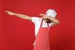 Young bearded male chef cook baker man in striped apron white t-shirt toque chefs hat posing isolated on red background in studio. Cooking food concept. Mock up copy space. Showing DAB dance gesture.