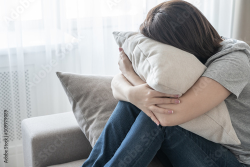 Cuadros en Lienzo Sad depressed woman at home sitting on couch and hugging a pillow, loneliness an