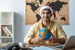 © LIGHTFIELD STUDIOS - handsome travel agent in santa hat holding globe while smiling at camera
