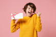 Joyful young brunette woman girl in yellow sweater posing isolated on pastel pink background studio portrait. People lifestyle concept. Mock up copy space. Hold gift certificate, doing winner gesture.