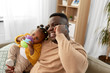 © Syda Productions - family, fatherhood and technology concept - happy african american father with baby at home calling on smartphone