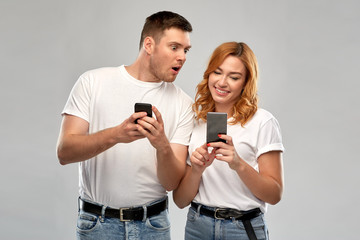 Poster - technology and people concept - happy couple in white t-shirts with smartphones over grey background