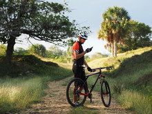 Sports, active lifestyle and modern technology. Outdoor picture of cyclist on mountain bike using navigator on smart phone, exploring map and searching GPS coordinates while biking in countryside.