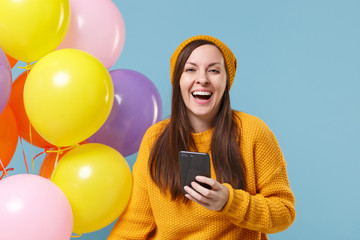 Sticker - Cheerful young woman in sweater hat posing isolated on blue background. Birthday holiday party, people emotions concept. Mock up copy space. Celebrating hold colorful air balloons using mobile phone.