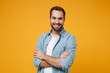 © ViDi Studio - Smiling young bearded man in casual blue shirt posing isolated on yellow orange wall background, studio portrait. People sincere emotions lifestyle concept. Mock up copy space. Holding hands crossed.