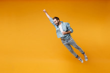 Funny Young Bearded Man In Casual Blue Shirt Posing Isolated On Yellow Orange Background, Studio Portrait. People Lifestyle Concept. Mock Up Copy Space. Jumping With Outstretched Hand Like Superman.