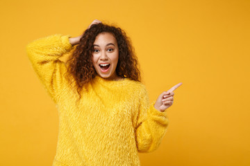 Excited young african american girl in fur sweater posing isolated on yellow orange wall background. People lifestyle concept. Mock up copy space. Putting hand on head, pointing index finger aside.