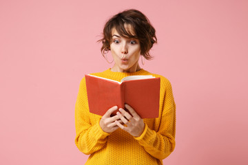 Wall Mural - Amazed young brunette woman girl in yellow sweater posing isolated on pink wall background, studio portrait. People sincere emotions lifestyle concept. Mock up copy space. Holding and reading book.