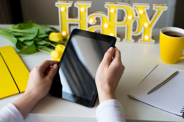 A business woman's hands using tablet with yellow neon with description Happy, yellow mug of coffee on white table, yellow design, yellow colors, buisiness background