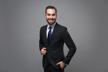 Wall Mural - Smiling young bearded business man in classic black suit shirt tie posing isolated on grey background studio portrait. Achievement career wealth business concept. Mock up copy space. Looking camera.