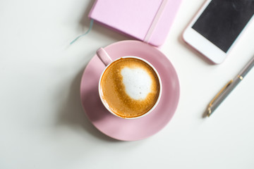 Pink notebook and cup of cappuccino coffee with pink tulips on white background. Pink writing set with cappuccino. Woman's workplace in pink. Flat lay. Top view. Copy space