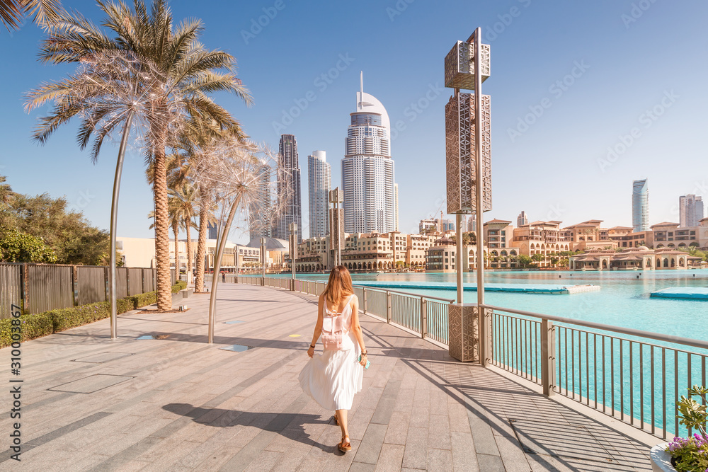 Happy tourist girl walking near fountains in Dubai city. Vacation and sightseeing concept - obrazy, fototapety, plakaty 