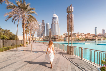 happy tourist girl walking near fountains in dubai city. vacation and sightseeing concept