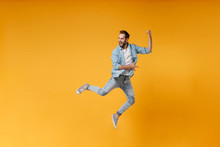 Funny Young Bearded Man In Casual Blue Shirt Posing Isolated On Yellow Orange Wall Background Studio Portrait. People Lifestyle Concept. Mock Up Copy Space. Jumping Fooling Around Like Playing Guitar.