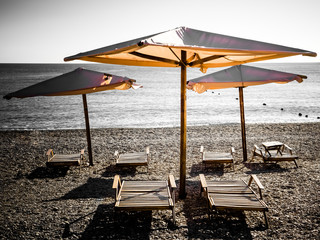 Wall Mural - Sun umbrellas and wooden beach beds on the sea pebble beach.