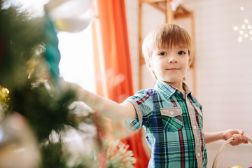 Wall Mural - Cute little boy of about five year with blue eyes decorating a Christmas tree.