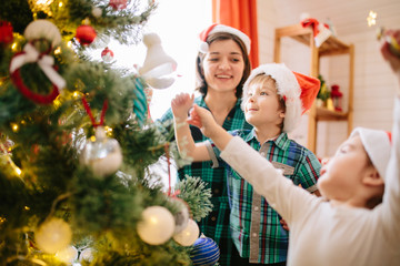 Wall Mural - Happy family mom, son and daughter on a Christmas winter sunny morning in a decorated Christmas celebration room with a Xmas tree and gifts.