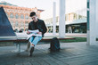 © GalakticDreamer - Smiling student working with papers and sitting on bench with laptop