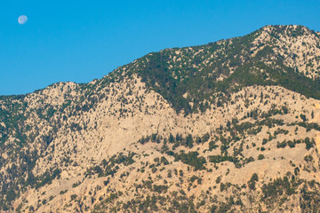 daytime bright light of the mountains with sand cover and the moon on a blue sky