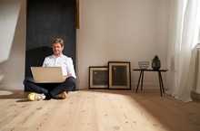 Relaxed Mature Man Sitting On The Floor At Home Using Laptop