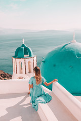 Wall Mural - Young woman with blonde hair and blue dress in oia, santorini, greece with ocean view and churches