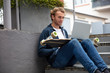 © Westend61 - Young man sitting on steps, using laptop on longboard