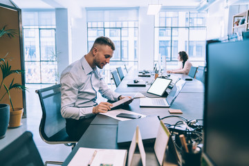 delighted male surfing laptop and tablet in open space while analyzing statistics